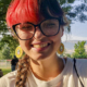Girl with red hair and glasses smiling.